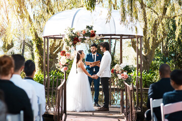 Wall Mural - Stepping into holy matrimony. Cropped shot of a handsome young male marriage officiant joining a young couple in marriage outdoors.