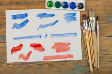 Poster - Paint brushes on old wooden background with colorful stroke on white paper