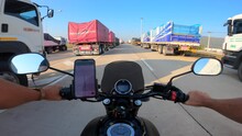 Point Of View Caucasian Man Using Google Maps Iphone Driving A Yamaha Motorcycle On A Highway With Many Semi Trucks Parked In Thailand.