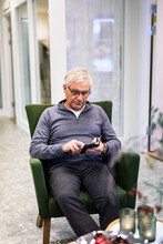Senior Man Sitting In Armchair And Using Smart Phone