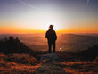 Man with a hat standing on a mountain peak and enjoying a beautiful landscape during sunset