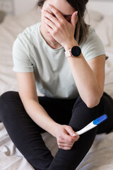 Wall Mural - the woman found out about an unwanted pregnancy. A woman with a pregnancy test in her hands is sitting on the bed in her apartment