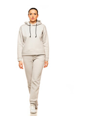 Wall Mural - Front view of a young woman in a gray tracksuit and hood walking to a white background in the studio