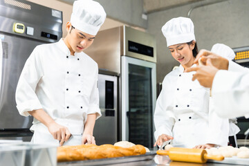 Smiling  asian  female bakers looking at camera..Chefs  baker in a chef dress and hat, cooking together in kitchen.Team of professional cooks in uniform preparing meals  in the kitchen.