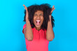 Young girl with afro hairstyle wearing pink t-shirt over blue background goes crazy as head goes around feels stressed because of horrible situation