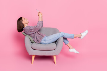 Wall Mural - profile side view portrait of attractive cheerful girl sitting in armchair using device isolated ove