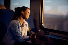 Young Happy Woman Looks Through Window While Traveling By Train At Sunset.