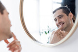 Fototapeta Do pokoju - happy and shirtless man smiling while looking at mirror in bathroom.