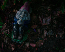 Top View Of A Colorful Sleeping Gnome Statue On The Garden Ground Surrounded By Fallen Autumn Leaves
