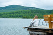 © Ermolaeva Olga - Mom hugs the child sitting next to her on the pier of a blue lake in the mountains and gently looks at the child. Family tourism