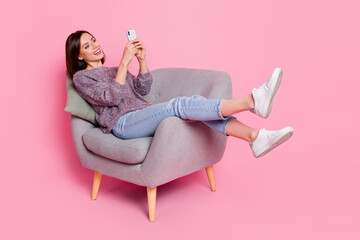 Wall Mural - portrait of attractive cheerful girl in armchair using device gadget smm isolated over pink pastel c