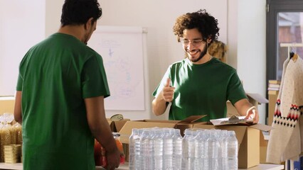 Wall Mural - charity, donation and volunteering concept - male volunteers with clipboard packing food and drinks in boxes over international group of people at distribution or refugee assistance center