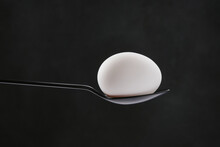 White Single Egg In A Black Spoon On Black Background. Selective Focus