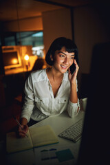 Aufkleber - Technology carries her through the night. Shot of a young businesswoman using a mobile phone and computer during a late night at work.