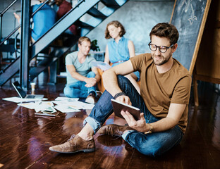 Poster - Using smart tools to gain a competitive edge. Shot of a young designer working on a digital tablet with his colleagues in the background.