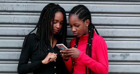 Canvas Print - African teen girls using cellphone together, Black teen girlfriends smiling and laughing holding smartphone