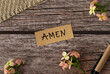Amen, handwritten text with uppercase letters in English on a wooden table with flowers and pen in vintage style. Top view, flat lay.