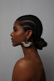 Close-up of African young woman with braids and earrings posing on grey wall.