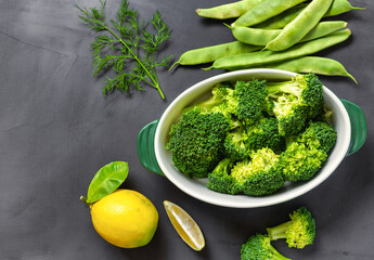 Poster - Raw ingredients for cooking healthy vegetarian food. Broccoli, green beans, lemon and parsley on a dark background top view