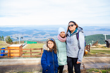 Wall Mural - Portrait of a happy family at the top with a view of mountain landscape on the autumn day. Mother with daughters in nature.