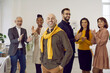 © Studio Romantic - Smiling business team leader. Happy confident successful handsome bald man in casual wear standing hands in pockets, with team of people applauding in background. Recognition at work, success concept