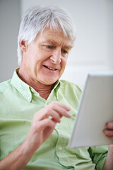 Wall Mural - Getting acquainted with technology. Shot of an elderly man using a digital tablet while sitting on the sofa at home.