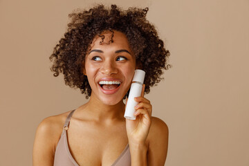 Cute woman holding cosmetic product in studio