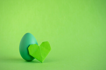 Easter egg and origami heart on green backgorund. Copy space.