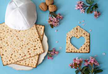 Wall Mural - Layout of Matzah shape of small house with heart,  matzo on plate, pink flowers and white kipa on blue background. Traditional of Jewish Holiday on Passover. Home symbol of happy family. Top view. 