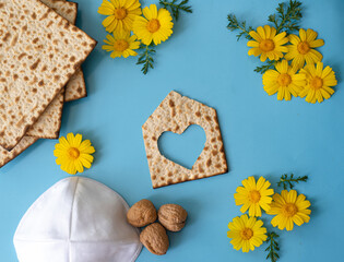 Wall Mural - Layout of Matzah shape of small house with heart,  matzo, flowers, white kipa and nuts on blue background. Traditional of Jewish Holiday on Passover. Home symbol of happy family. Top view. 