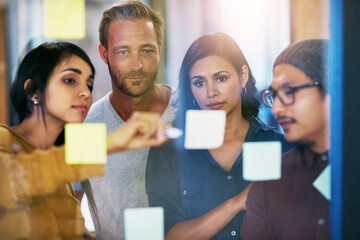 Canvas Print - Forming the best strategy together. Shot of a group of businesspeople brainstorming with notes on a glass wall in an office.