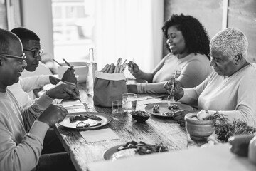 Wall Mural - Happy african family eating lunch together at home - Focus on mother face - Black and white editing