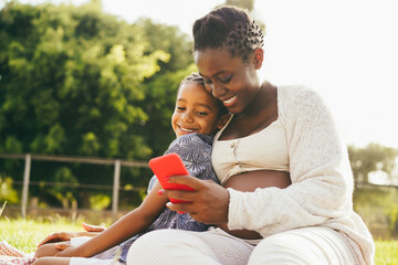 happy pregnant mother and son having fun using mobile phone outdoor - focus on mom face