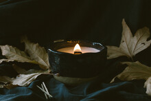 Lit Wooden Wick Candle With Fall Leaves And Dark Background