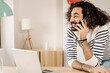 © Cavan Images - Cheerful man talking on phone with his laptop next to him at home