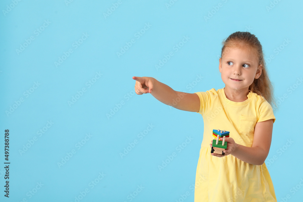 Cute little girl with building blocks pointing at something on blue background