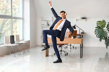 Wall Mural - Dancing young businessman with headphones in office