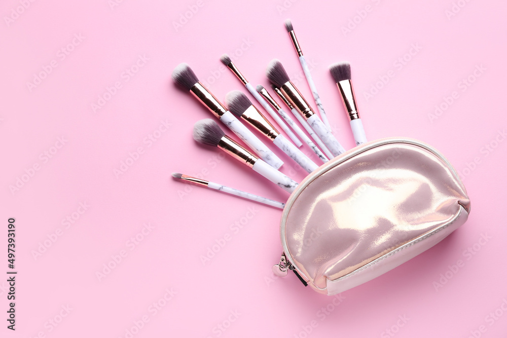 Bag with set of makeup brushes on pink background, top view