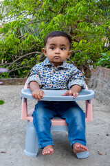 Wall Mural - T-shirt and jeans pants Wearing an infant sitting in a chair in the green garden. Baby's beautiful face on a beautiful afternoon. Asian cute baby boys portrait on rooftop.