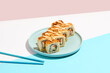 Tempura maki roll on ceramic plate with chopsticks. Hot sushi with salmon, crab and cucumber inside, spicy mayo topped. Modern japanese menu concept. Maki sushi on coloured background.