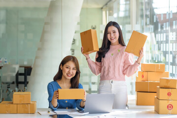 Two beautiful young Asian business owner woman prepare parcel box and check online orders of product for deliver to customer. Shopping Online concept.