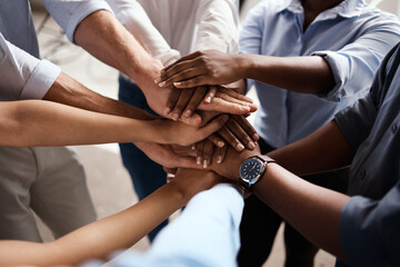 Poster - Were in this together. Shot of a group of unrecognizable businesspeople stacking their hands at work.