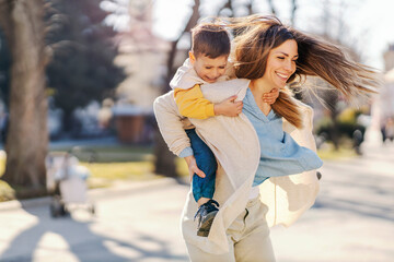 A mother and son having fun, spinning, having piggyback ride in a park.