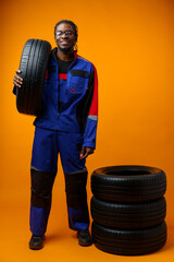 African american car service worker with car tyre against yellow background