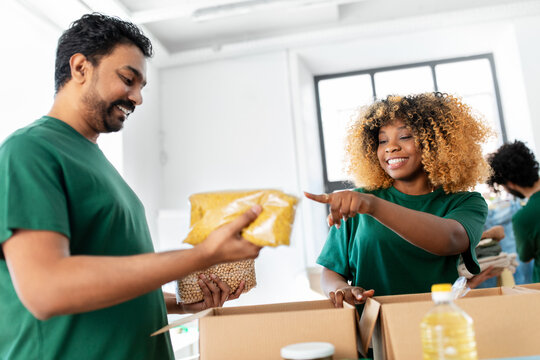 charity, donation and volunteering concept - international group of happy smiling volunteers packing food in boxes at distribution or refugee assistance center