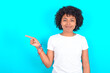© Jihan - young woman with afro hairstyle wearing white T-shirt against blue wall points to side on blank space demonstrates advertisement. People and promotion concept