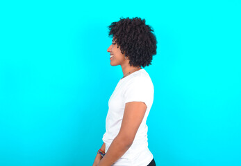 Profile portrait of nice young woman with afro hairstyle wearing white T-shirt against blue wall look empty space toothy smile