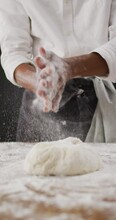 Vertical video of midsection of baker dusting hands with flour before kneading dough