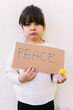 © Davidbenito - Serious, anti-war activist little girl holding a sign that reads: 'PEACE' and a yellow flower. Concept of war, confrontation, activism, peace and love.