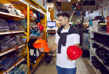 Wall Mural - Customer choosing a new hard hat at a modern DIY store or hardware shopping mall. Man who is planning to do some home repairs standing in the aisle, holding two hard hats and thinking which to take